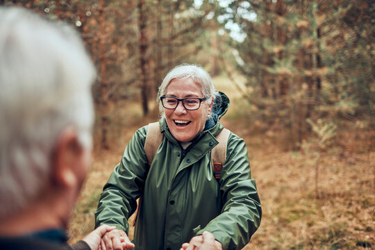 Senior woman laughing and holding hands on forest trail