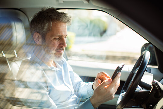 Mature man using smartphone in parked car