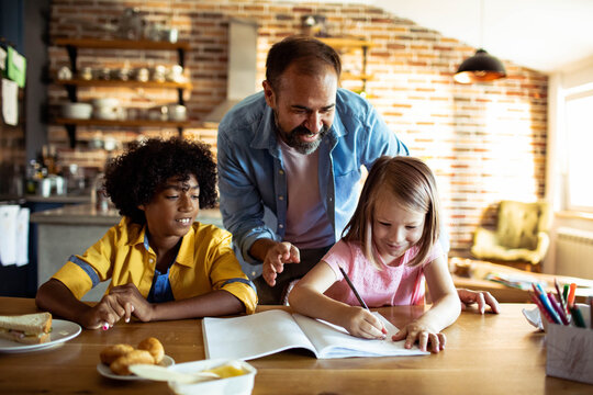 Parent helping children with homework at kitchen table