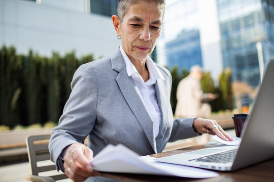 Senior businesswoman reviewing documents on laptop outdoors in city