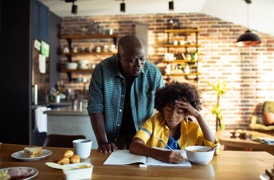 Older man helping boy with homework at kitchen table