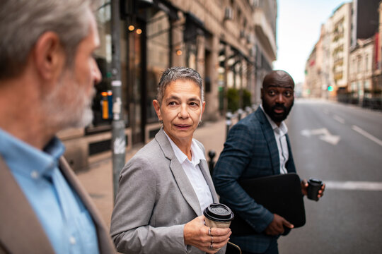 Diverse business colleagues with coffee crossing city street downtown