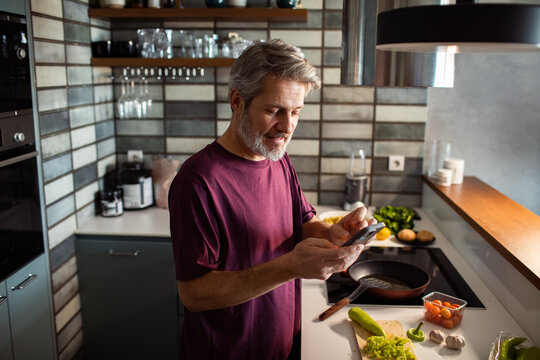 Mature man using smartphone while cooking in modern home kitchen