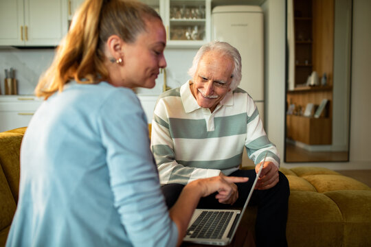 Young woman helping senior man with laptop at home