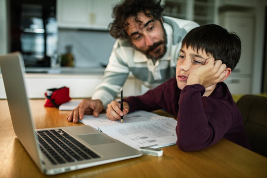 Father helping bored son with homework at kitchen table