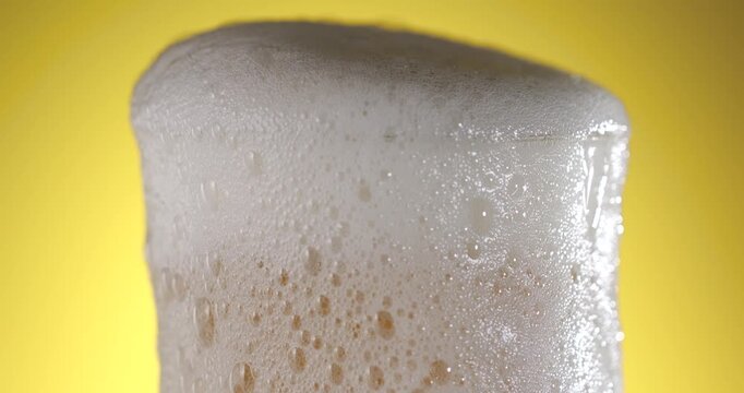 Slow motion of beer foam rising in a glass with bubbles and golden liquid