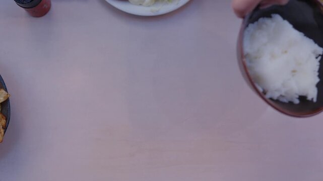 Hands set down plate of stir fried pork with cabbage and bowl of rice Japan