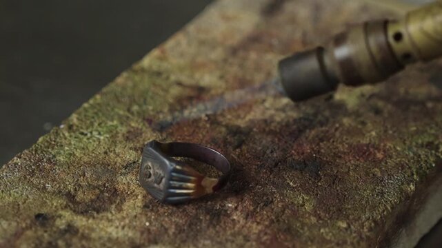 Gold signet ring heated by a blue torch flame on a jewellers soldering bench