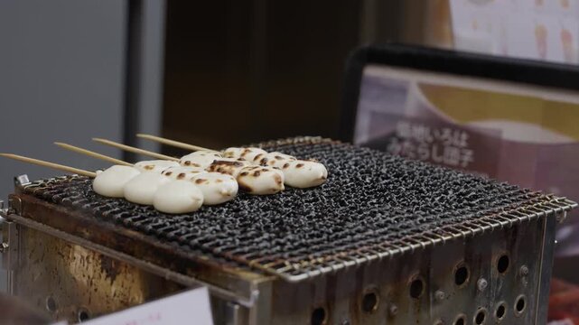 Vendor grilling dango rice dumpling skewers over a charcoal grill at an open air Tokyo market