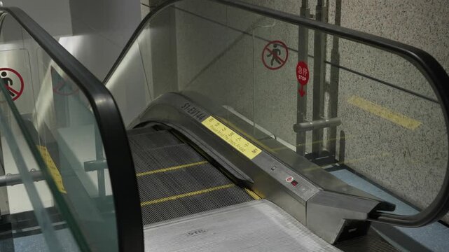 Bottom of a stainless steel escalator with a No Walking warning sign on a wall at a Chinese airport