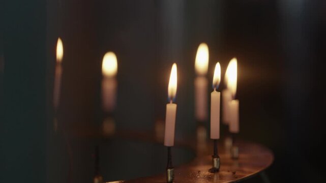 Row of thin lit candles glowing on a brass stand in the warm darkness of a Japanese temple