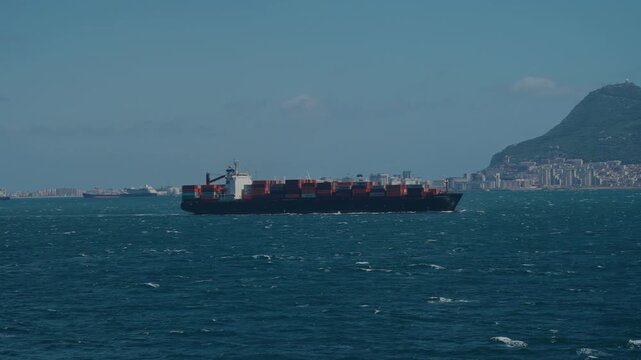 Container ship crossing the Strait of Gibraltar with the Rock and coastal town behind