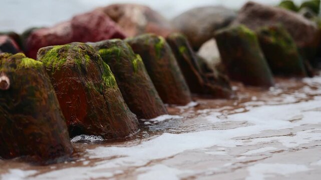 Wooden groyne and protective rocks on sandy beach. Seascape with breakwater extending into stormy sea. Erosion control structure on coastline. Natural scenery for travel concept.