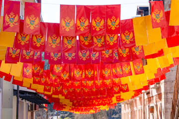 Fototapeta premium Bright red and yellow Montenegro national flags hanging in rows above a town street during a festive holiday