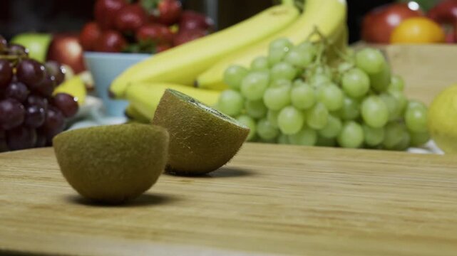 Cook slicing through delicious kiwi on cutting board near other fruit - closeup tracking shot
