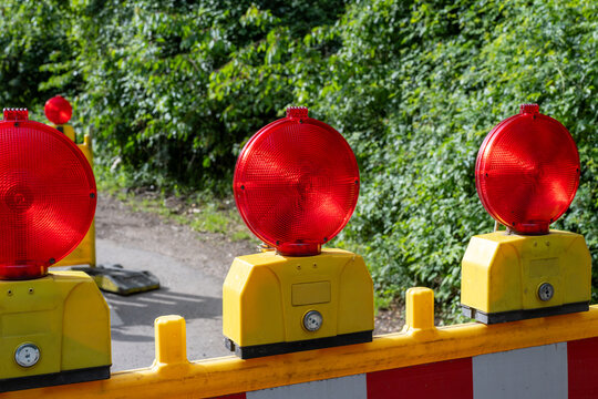 Three warning lights on orange barrier, green trees behind