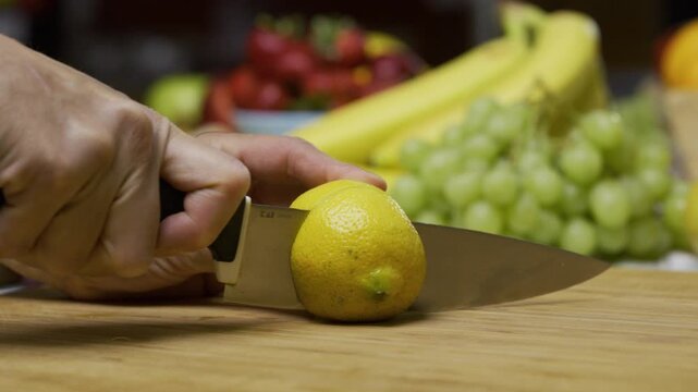 Cook using sharp knife to slice through juicy lemon on cutting board - closeup slow motion shot