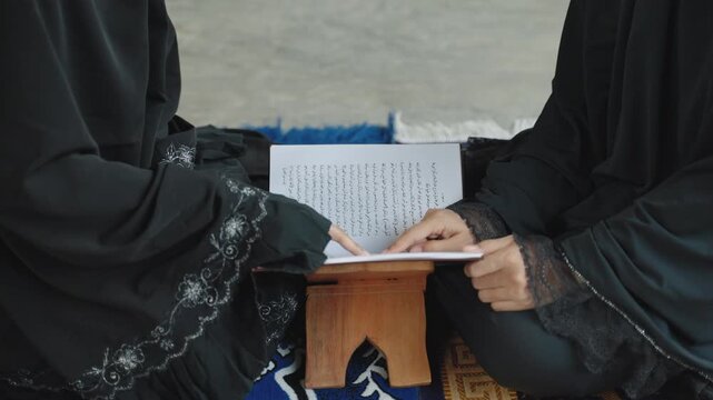 Two Muslim women reading and discussing the Quran together while seated on a prayer mat. Islamic education, faith, spiritual learning, and religious study concept.
