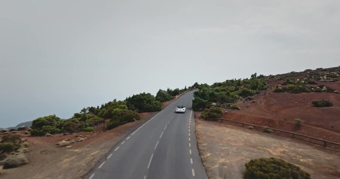 Convertible car traveling along a winding mountain road through a dramatic volcanic landscape under a cloudy sky, showcasing a sense of adventure, freedom, and discovery on a road trip to Tenerife