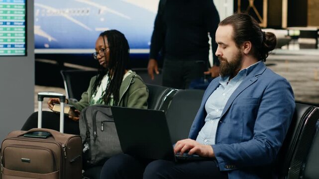 An entrepreneur types on a laptop and checks a mobile phone impatiently in an airport lounge, awaiting important notifications during a delegated business trip.