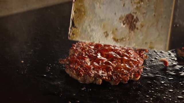 Metal spatula lifts and flipping sizzling burger patty from hot griddle