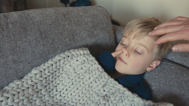 Father touching forehead of sick son resting on sofa