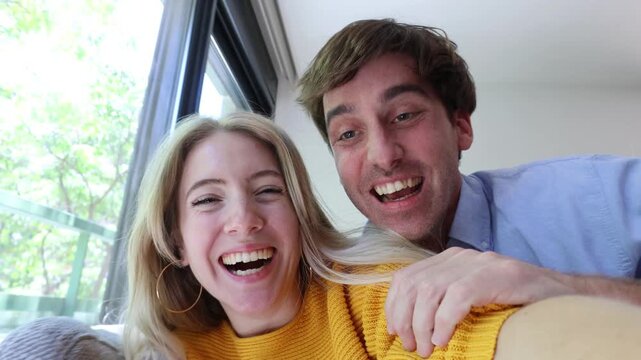 Joyful young couple running into their new apartment, laughing and celebrating as they take a selfie video. They happily wave at the camera, sharing their exciting moving day moment