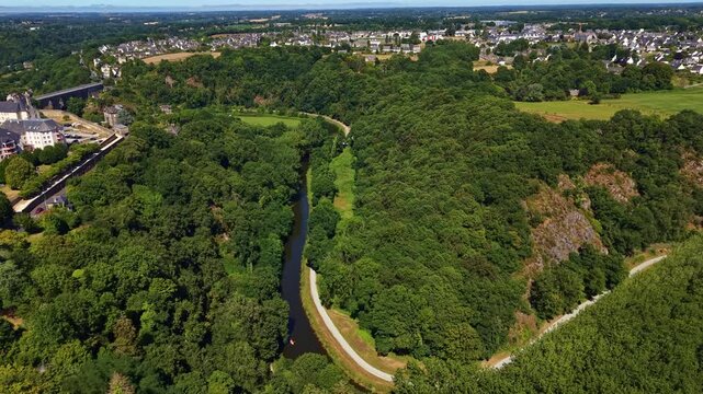 La Rance river flowing through lush green forest and valley near historic town in Dinan, France. Aerial drone panoramic view