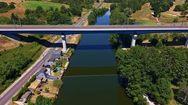 Modern concrete bridge over calm Mayenne river surrounded by green trees in France. Aerial drone view
