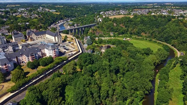 La Rance river flowing through lush green valley with historic Dinan viaduct in background in Brittany, France. Aerial drone forward