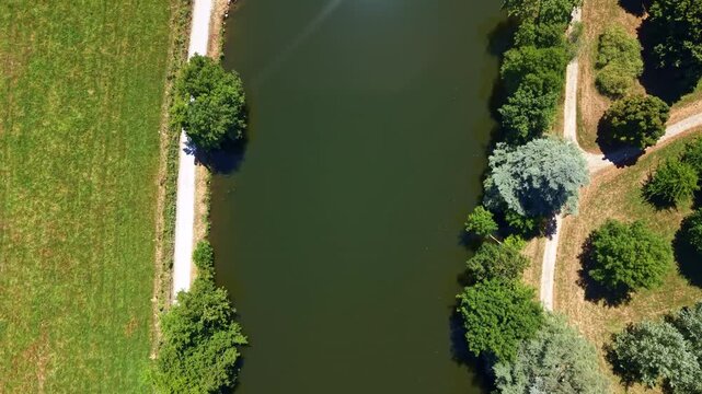 Drone top-down view above the Mayenne River bordered by trees, paths and farmland in western France.