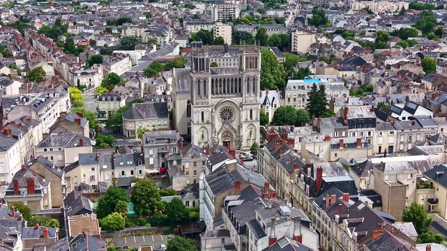 Drone pulling back from Saint Joseph Church, revealing surrounding streets, rooftops and the urban landscape of Angers, France.