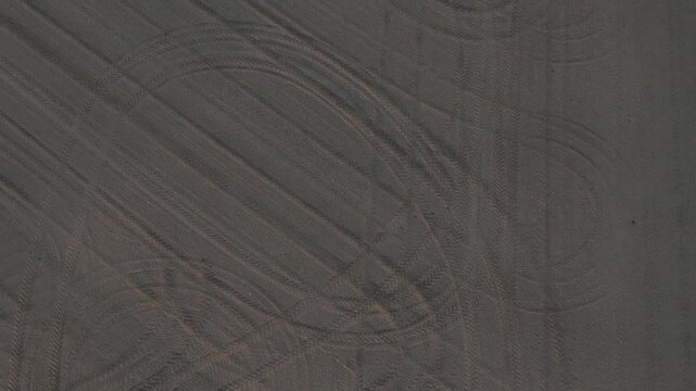 Freshly tilled seedbed in the Po Valley, Emilia-Romagna, Italy, shows fine harrowed soil and intersecting tractor tire tracks prepared for crop sowing, top down drone flyover.