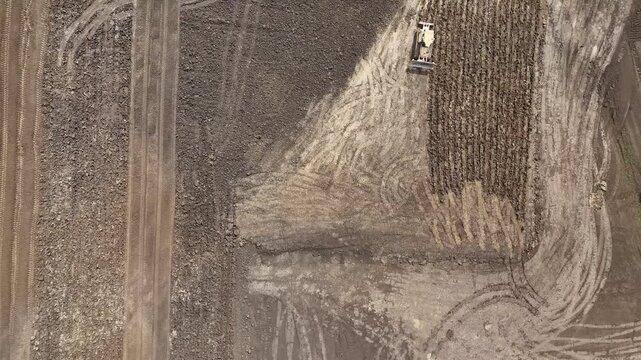 Crawler bulldozer performs bulk earthmoving across a datacenter construction site with graded platforms, haul roads and stripped topsoil, top-down flyover.
