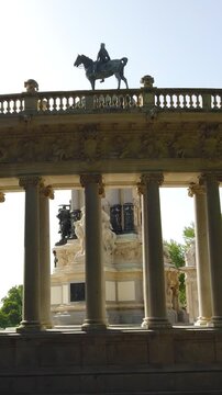 Ornate monument with equestrian statue framed by columns in a sunny city park
