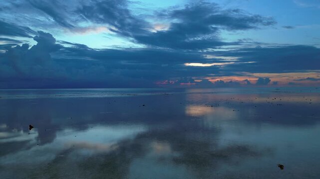 Calm ocean water reflecting a dramatic cloudy sky during a peaceful sunset creating a serene atmospheric landscape. Nice aerial view fly reverse drone panorama speed ramp hyper motion time lapse