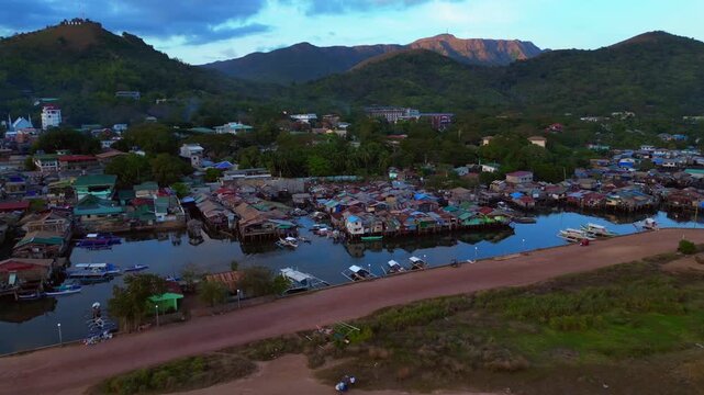 dense stilt floating houses built over water next to a pier, representing community and traditional living. Magic aerial view fly reverse drone panorama