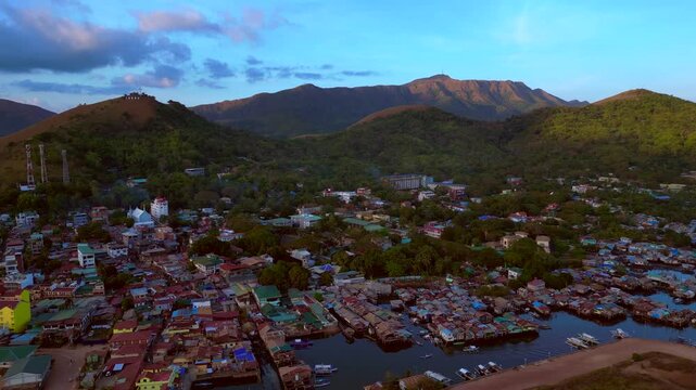 dense stilt floating houses built over water next to a pier, representing community and traditional living. Dramatic aerial view fly push forward drone panorama