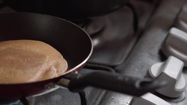 Closeup of pancake cooking in frying pan on gas stove. Golden surface rising as heat cooks the pancake with soft texture during food preparation in kitchen