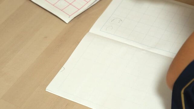 Close-up of a child's hands writing in a notebook with a pencil at a desk