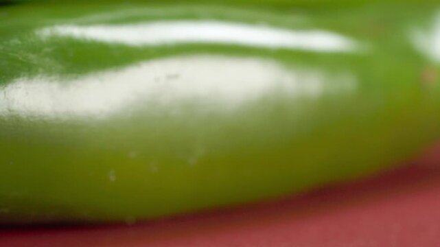 Extreme closeup of fresh green chili pepper stem and glossy surface against a red background. Macro view highlights natural texture, vibrant color and fine details of the vegetable