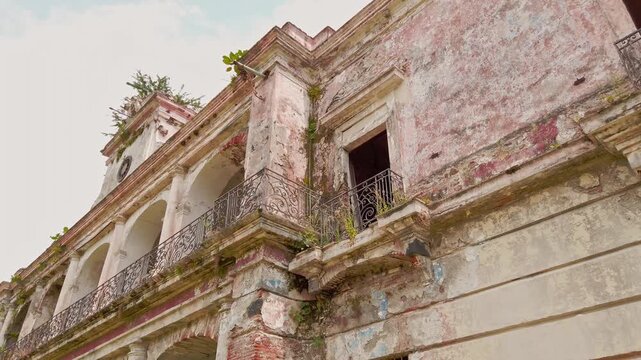 Low angle view of abandoned Hacienda Oacalco featuring weathered colonial facade, balconies and decaying architecture during daytime in Morelos, Mexico.