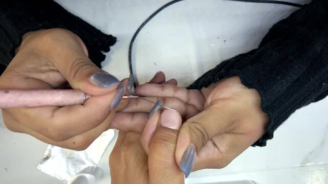 Top view of nail technician applying acrylic nail extension with precision electric drill during professional manicure treatment at beauty salon in Mexico