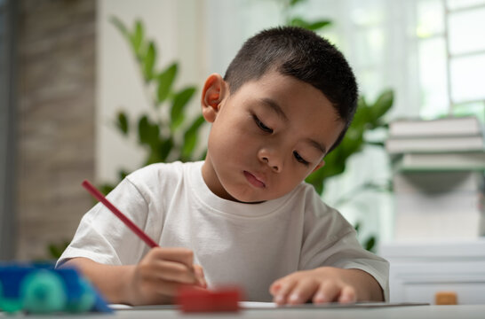Focused young child writing with a colored pencil at home, representing early learning, literacy development, concentration, fine motor skills, education, homeschooling, and academic growth.