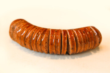 Naklejka premium A savory curved sausage precisely sliced along its length, displayed on a clean white surface.