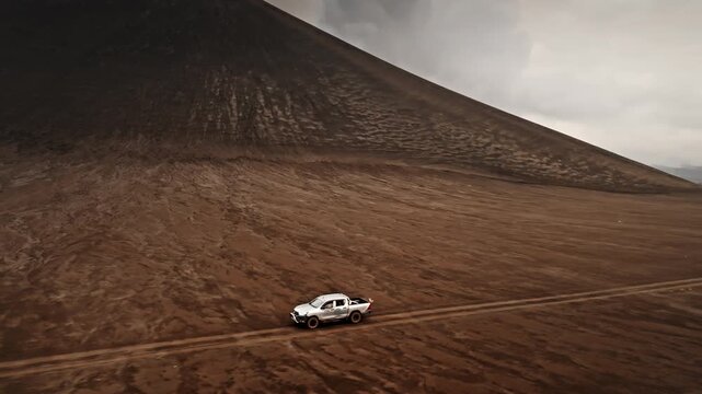 Pickup truck driving on a rugged dirt road along the base of an active stratovolcano. Creating a sense of adventure, exploration and travel in a remote and extreme landscape of ash and volcanic rock
