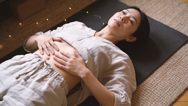 Woman practicing mindful belly breathing. Female doing somatic self-care on yoga mat.