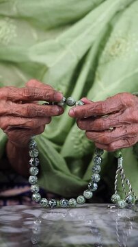 Elderly Person Praying with Green Prayer Beads