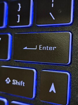 Close-up of backlit computer keyboard enter key focusing on blue lighting with keyboard, computer