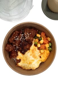 Top view of a delicious beef rice bowl served with fried egg and mixed vegetables in a paper bowl
